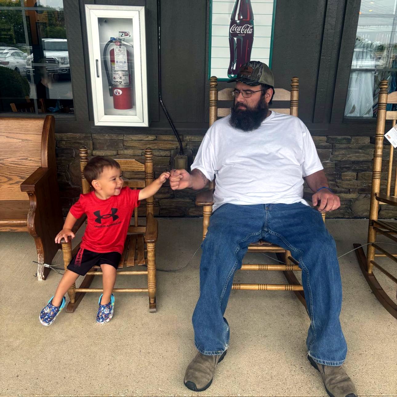 Timmy sitting with his young son, sharing a fist bump on rocking chairs.